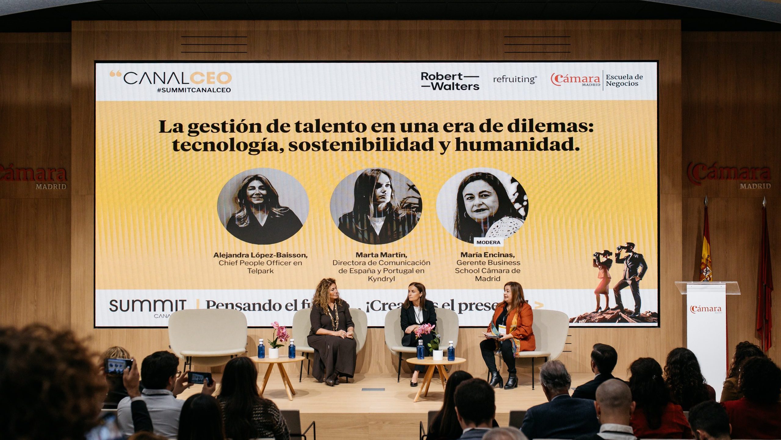 Foto abierta del escenario con 3 ponentes y publico